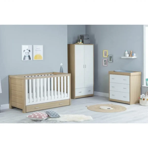 Modern nursery room with a wooden crib, white wardrobe, dresser with a changing table, wall shelf, and framed artworks on a gray wall, featuring a light gray rug and decorative pillows on the wooden floor.