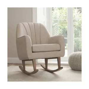 Beige upholstered rocking chair with wooden rockers in a bright room with large windows.