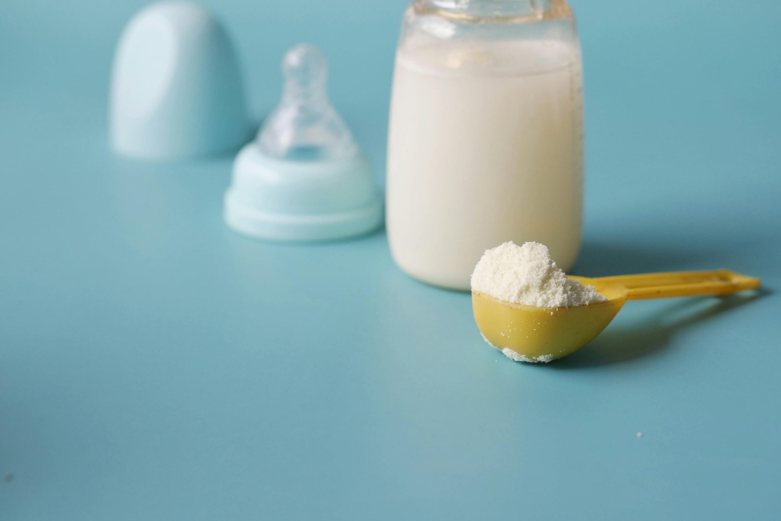 Formula Feeding: A yellow spoon filled with powdered formula is placed on a blue surface, with a baby bottle and its nipple cap in the background.