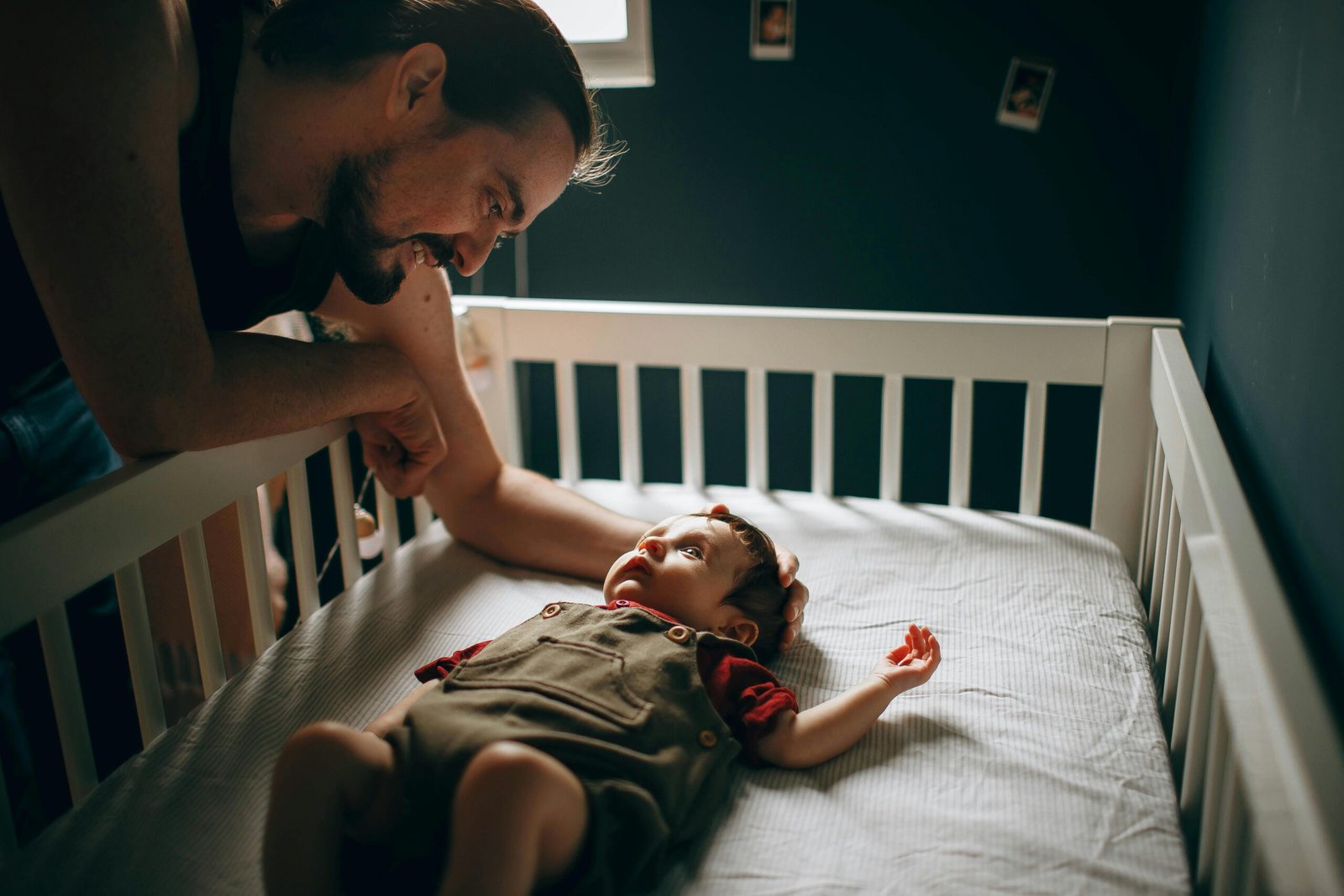 Your Guide to Safe Sleep for Baby (2025 Update) 3 A man leaning over a crib, smiling at a baby lying inside. The baby is wearing a brown dungaree and red shirt.