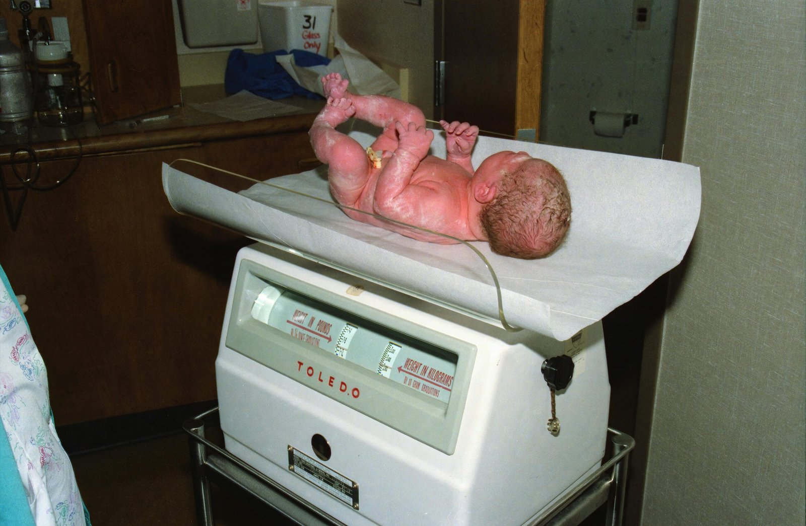 Understanding Newborn Birth Weight: A newborn baby lying on its back on a hospital scale covered with paper, in a medical setting.